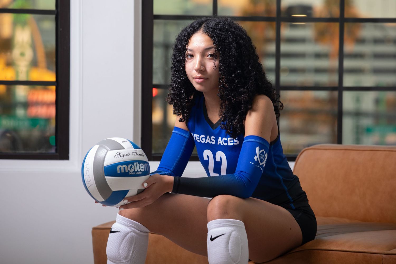 An athlete in a Vegas Aces uniform sits on a couch holding a volleyball.