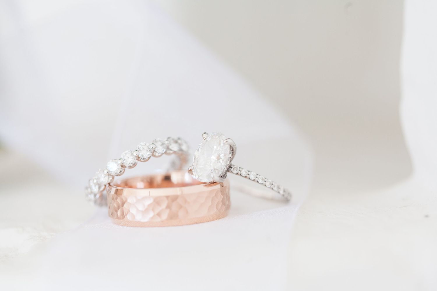 A diamond engagement ring and rose gold wedding band displayed together on white fabric.