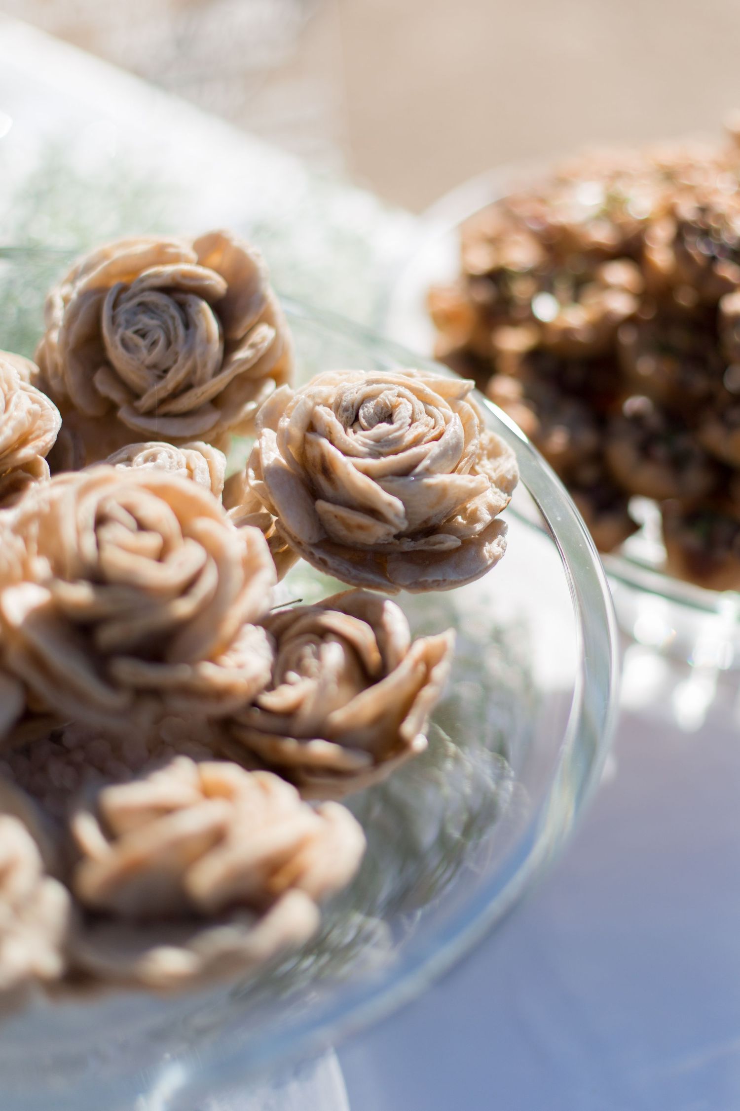 Delicate beige chocolate roses displayed on a glass cake stand at a wedding dessert table.