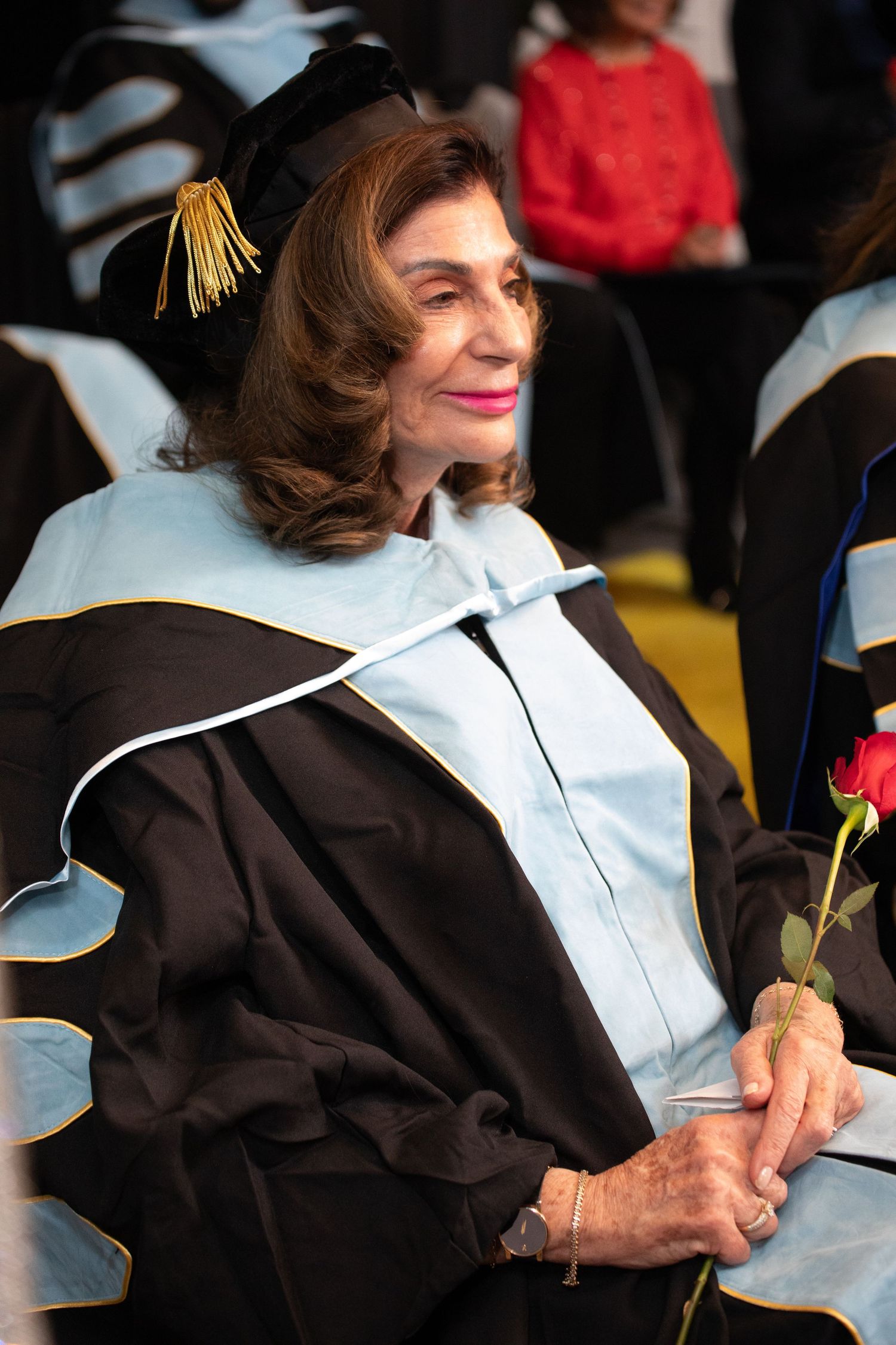 Graduate in academic regalia holding a red rose during commencement ceremony.