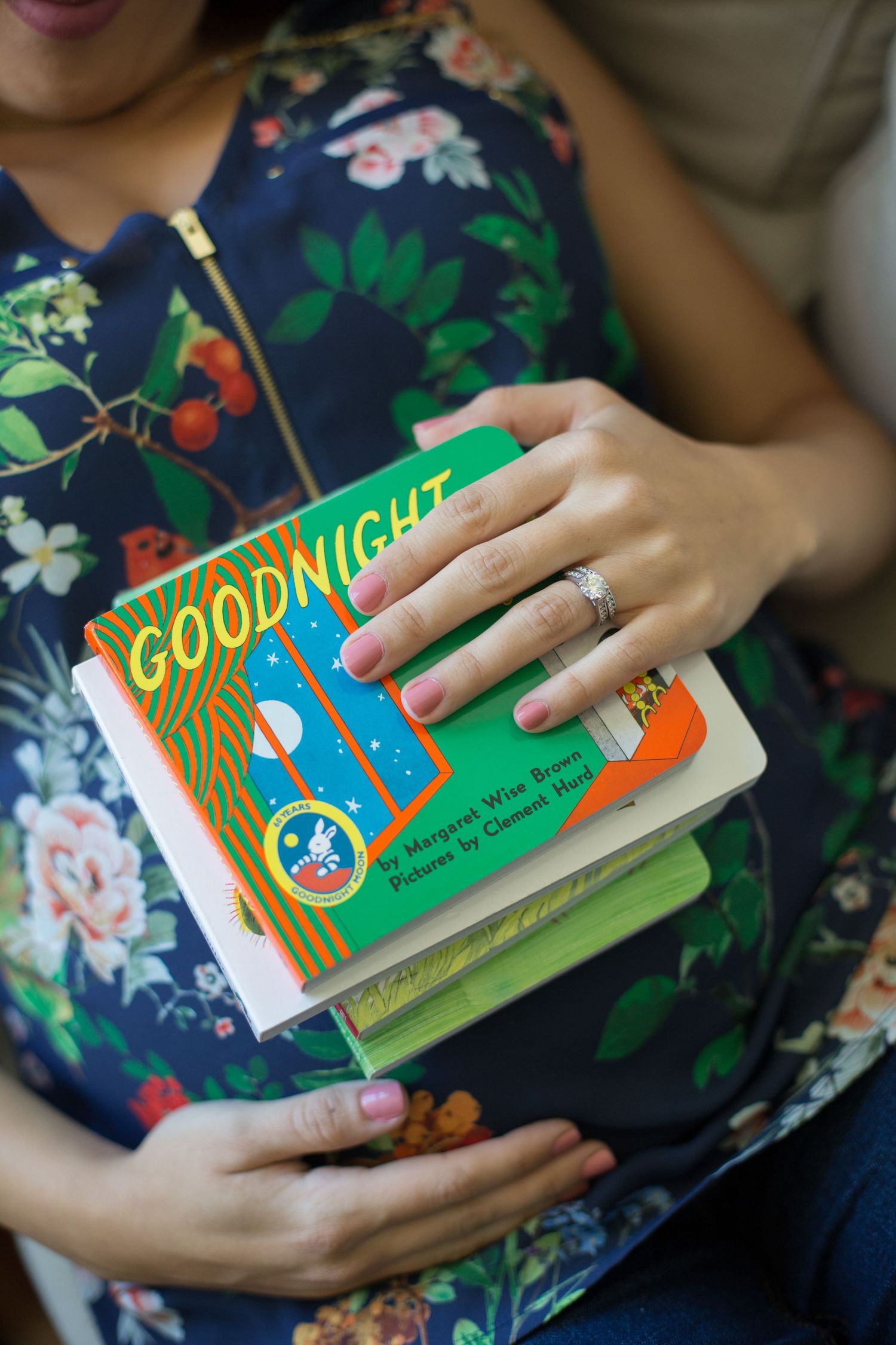 Floral dress-clad figure holds children's 'Goodnight' book against pregnant belly.