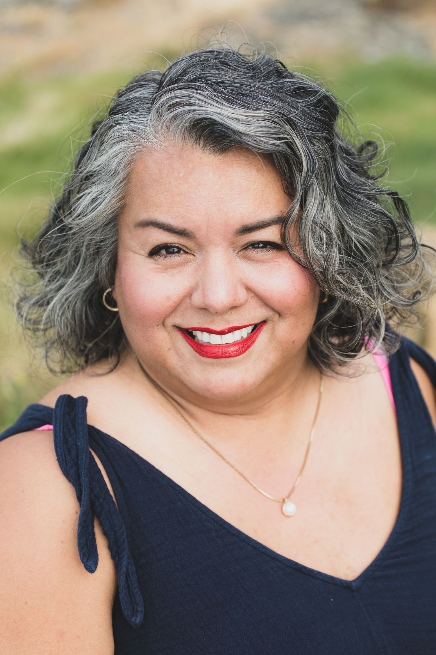 Closeup portrait showing silver curls, red lipstick and navy dress against outdoor background.