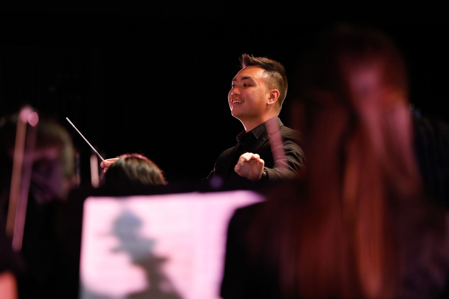 Orchestra conductor energetically directs musicians in dramatic lighting during performance.