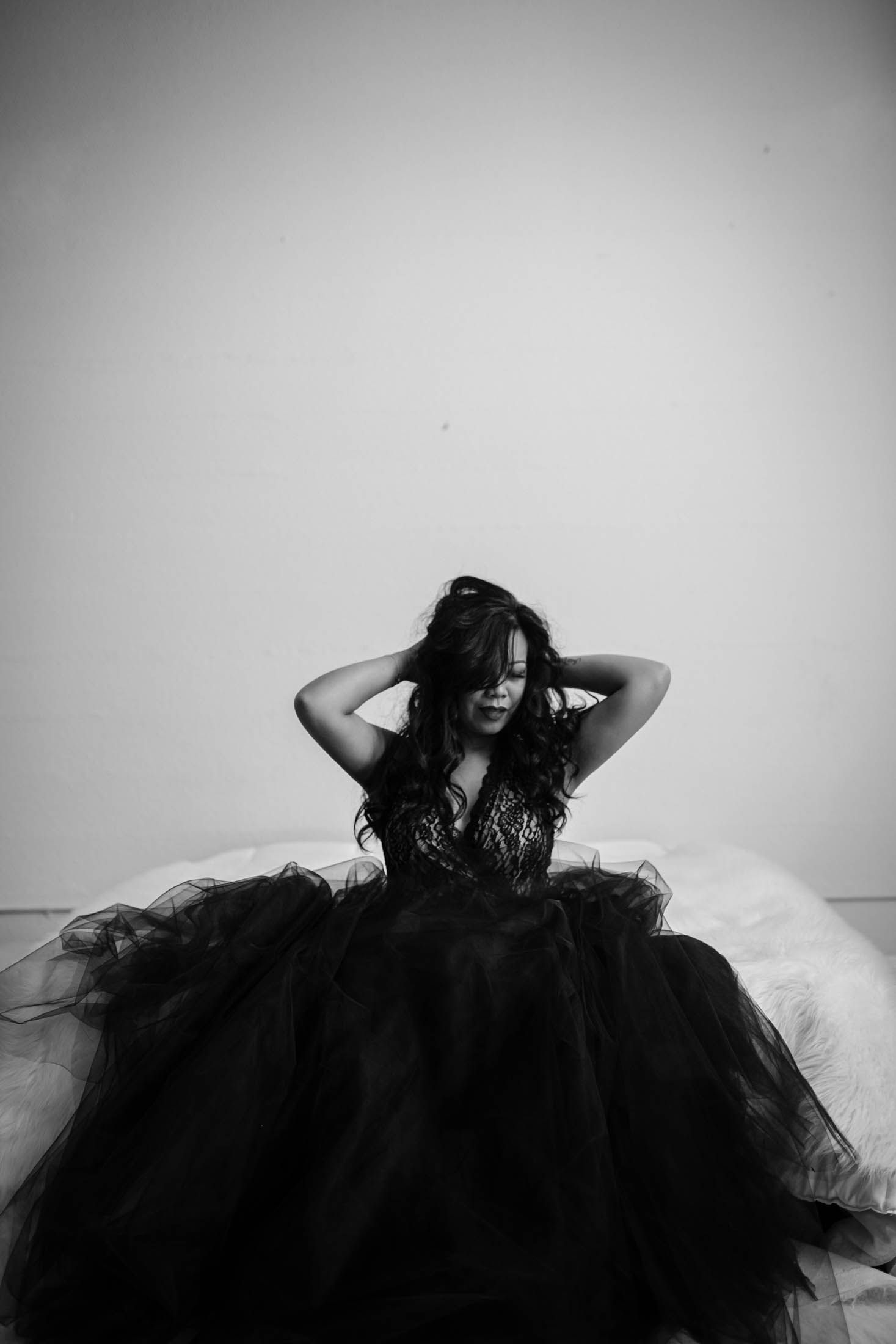 Dramatic black and white portrait of person in black tulle gown against light background.