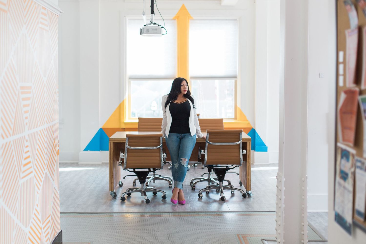 Professional standing in modern office space with directional arrows and office chairs.