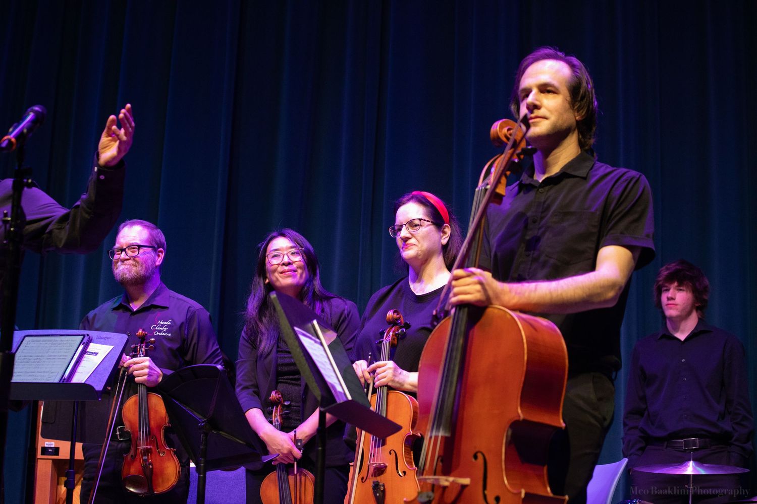 Classical music ensemble performs with cellos and string instruments on formal stage setting.