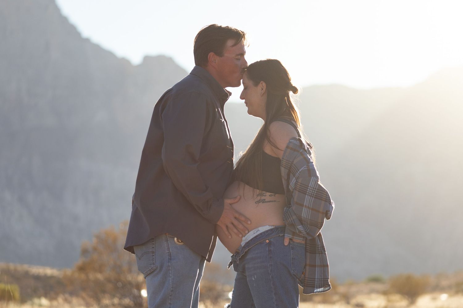 Couple sharing an intimate moment during maternity photoshoot with mountains in background.
