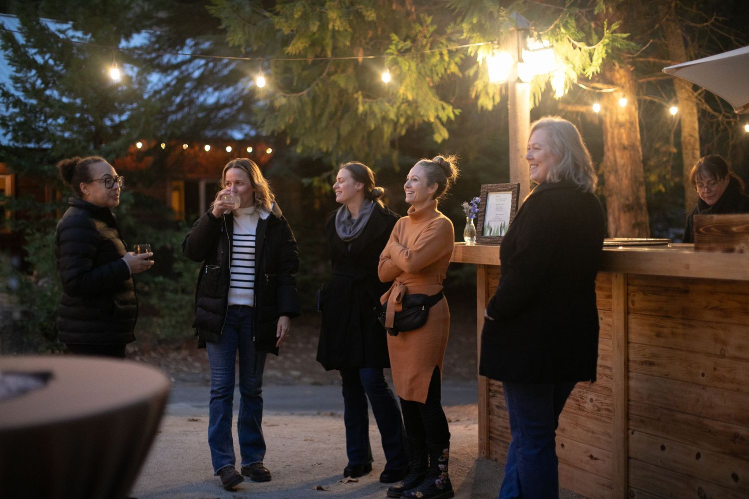 Evening outdoor gathering with string lights and guests enjoying drinks at bar.