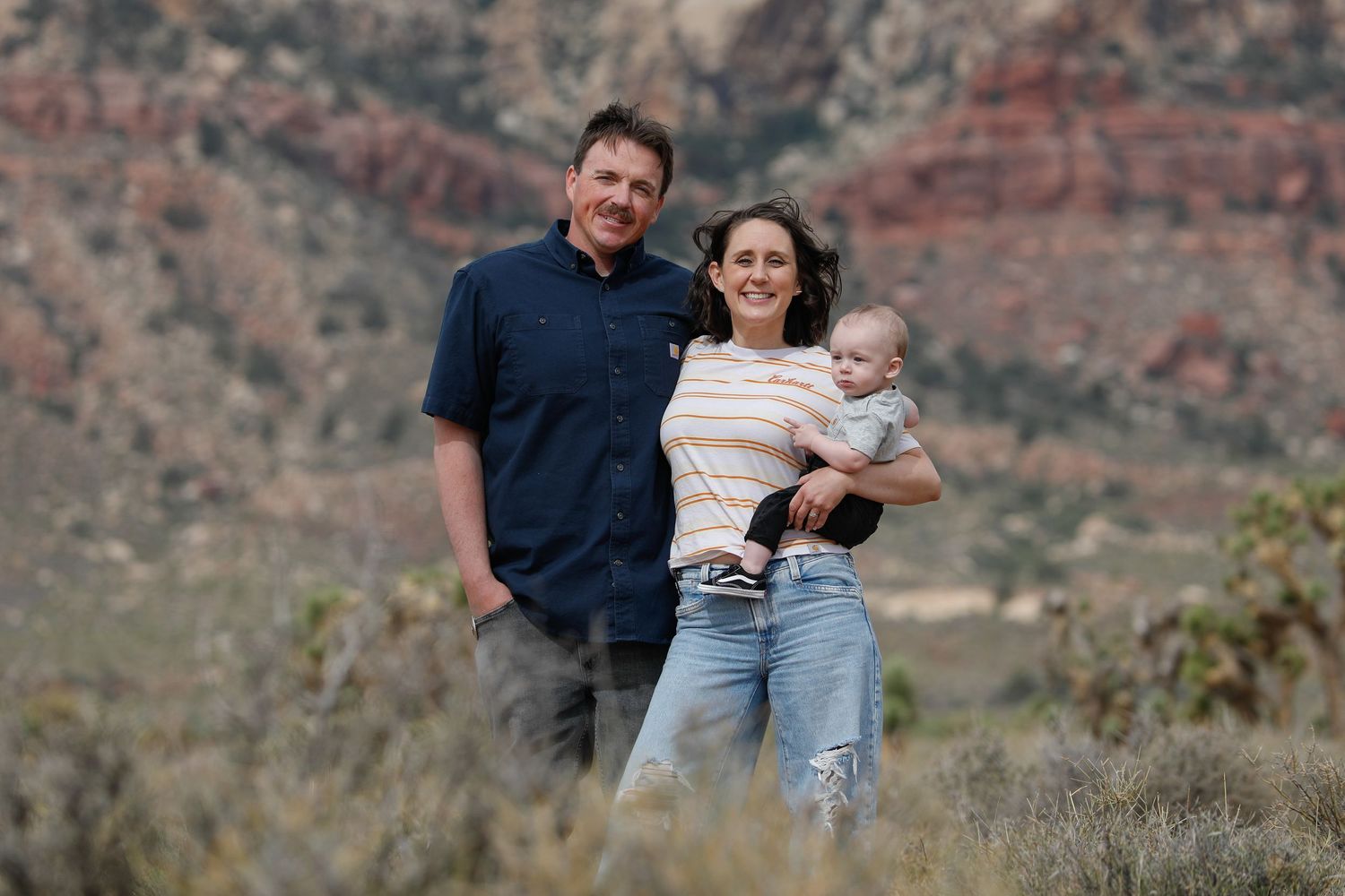 Family of three poses together against red rock canyon landscape.