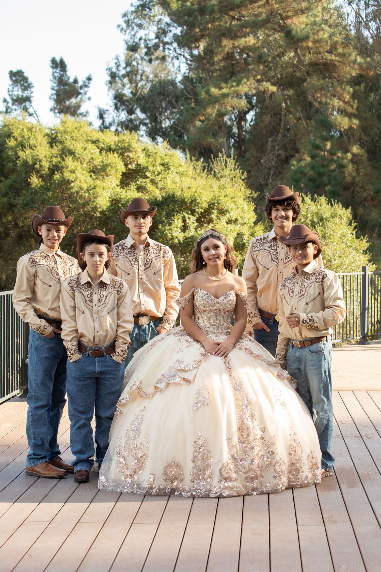 A quinceañera celebration photo with the celebrant in a gold-detailed gown surrounded by traditionally dressed escorts.