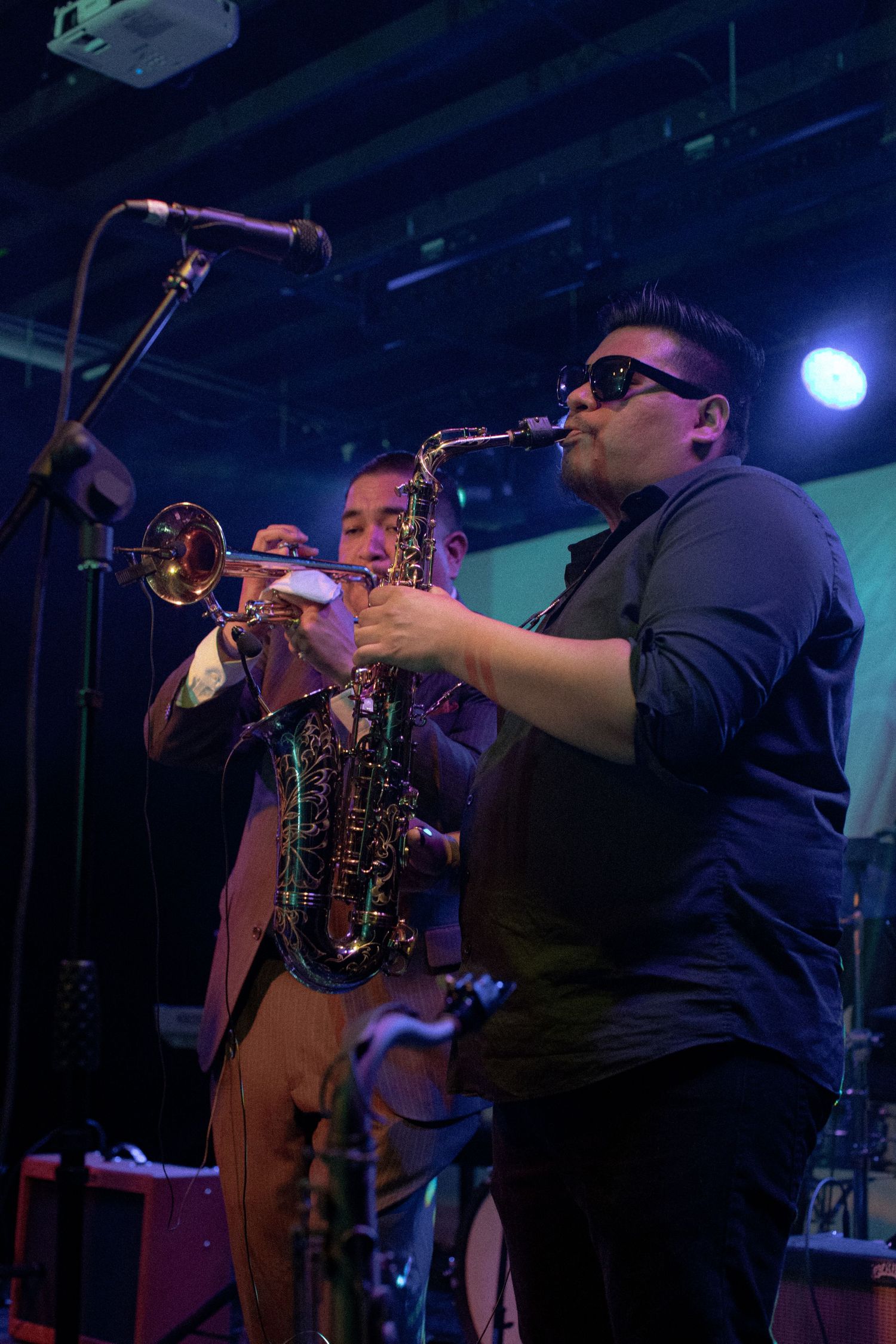 Jazz musicians perform on stage with trumpet and saxophone under blue stage lighting.
