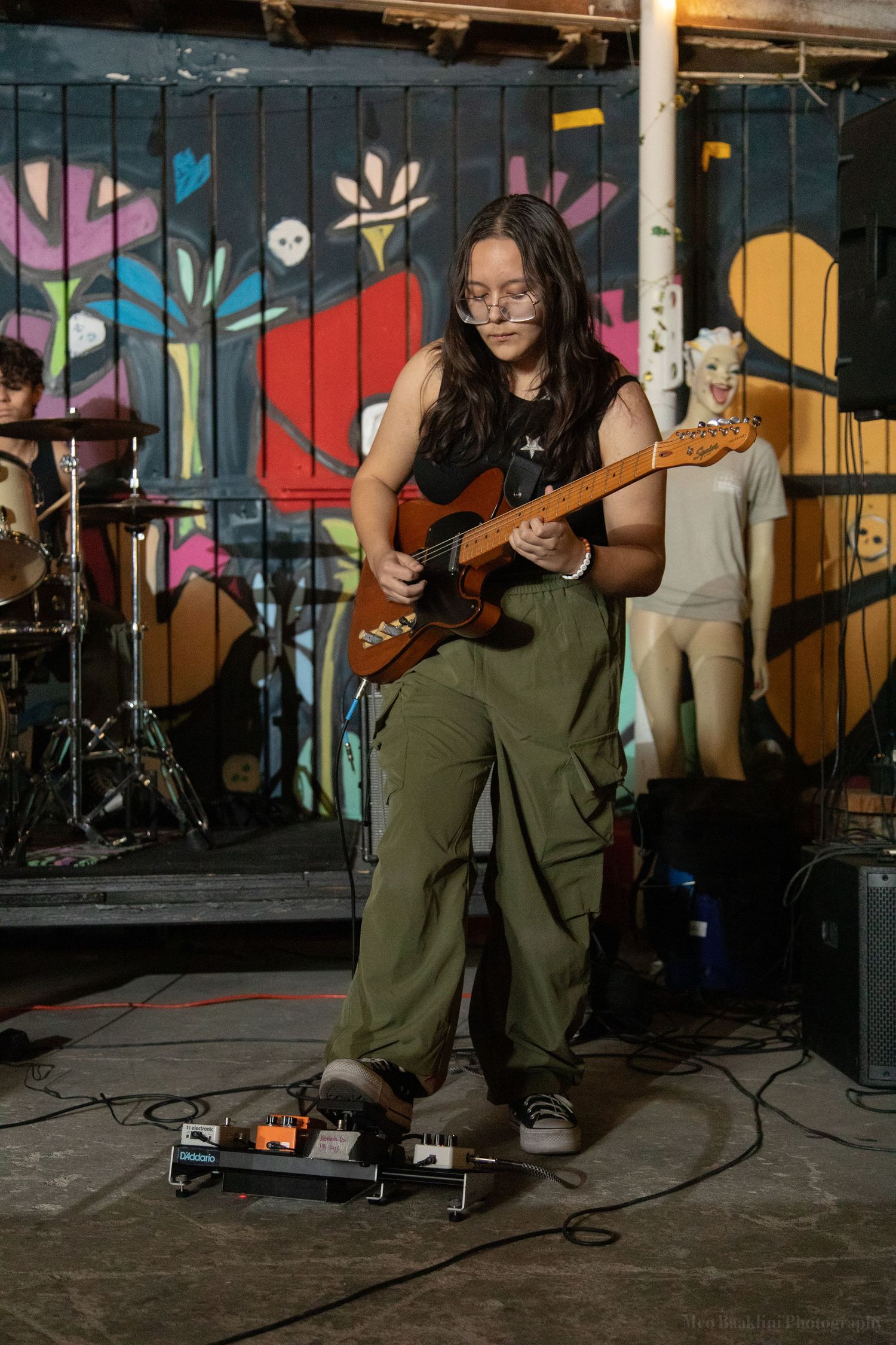 Musicians performing with guitars against colorful mural backdrop.