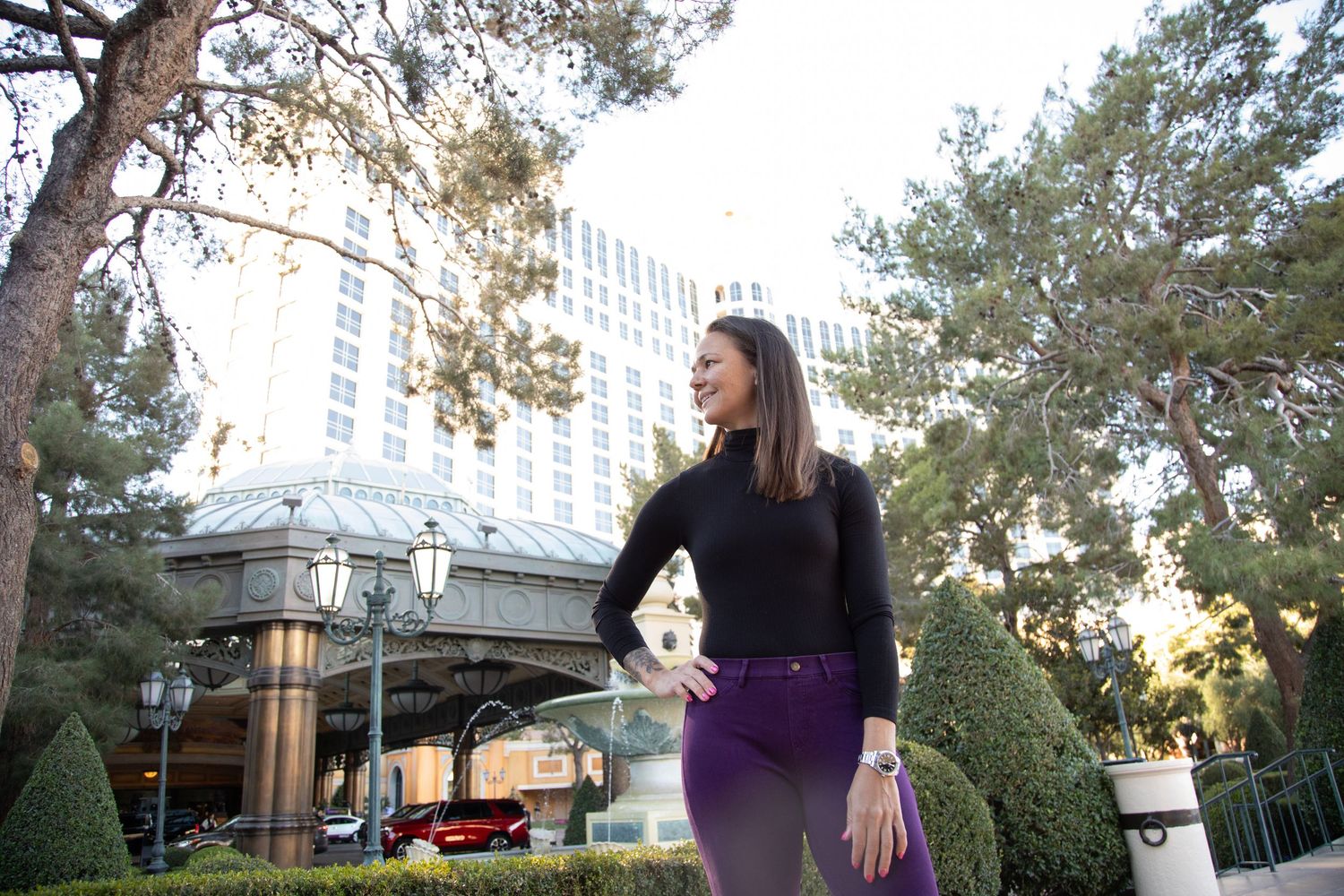 Woman in black sweater walking outside Caesars Palace hotel at sunset.