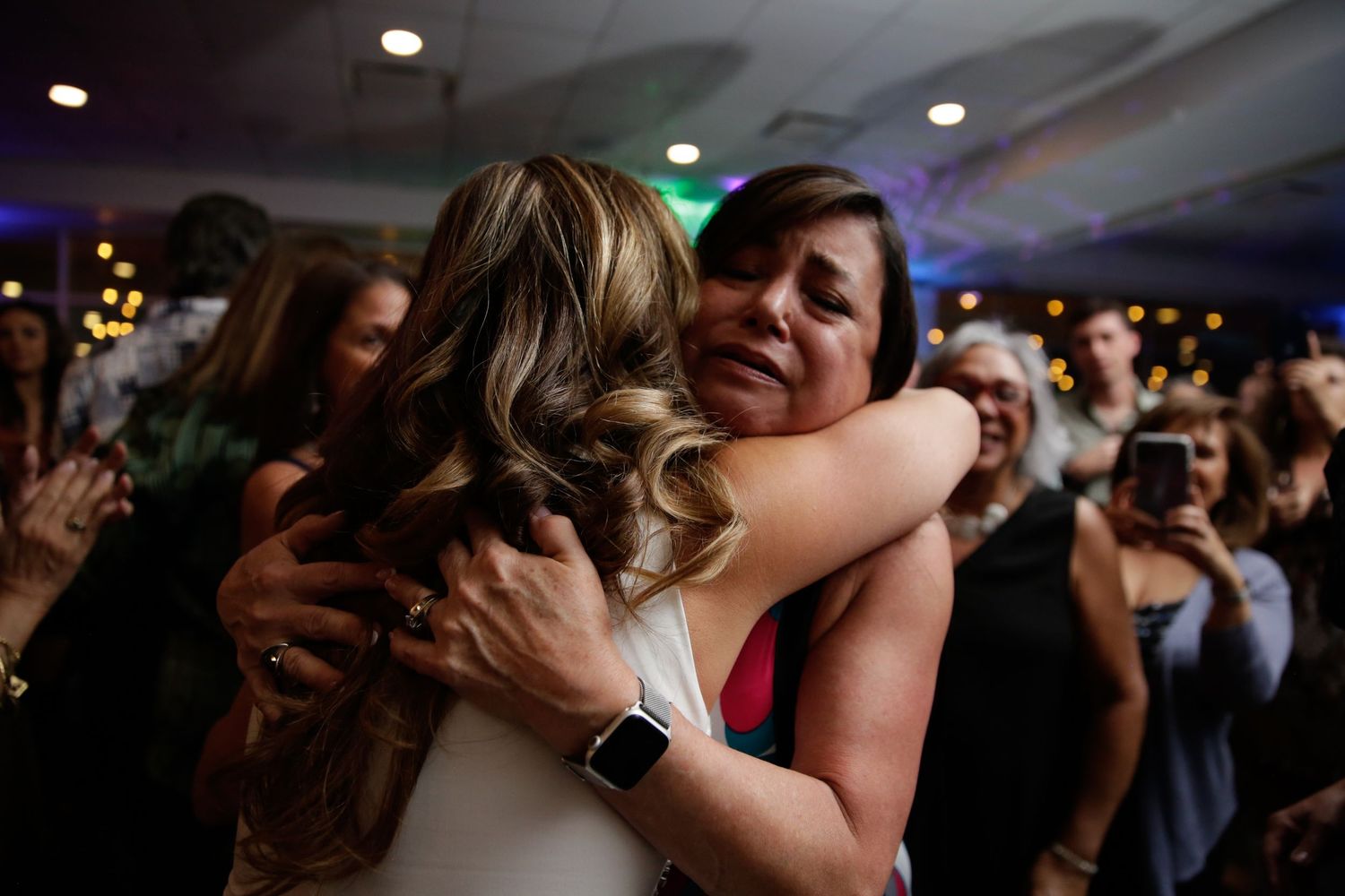 Emotional embrace between party attendees in dimly lit celebration setting.