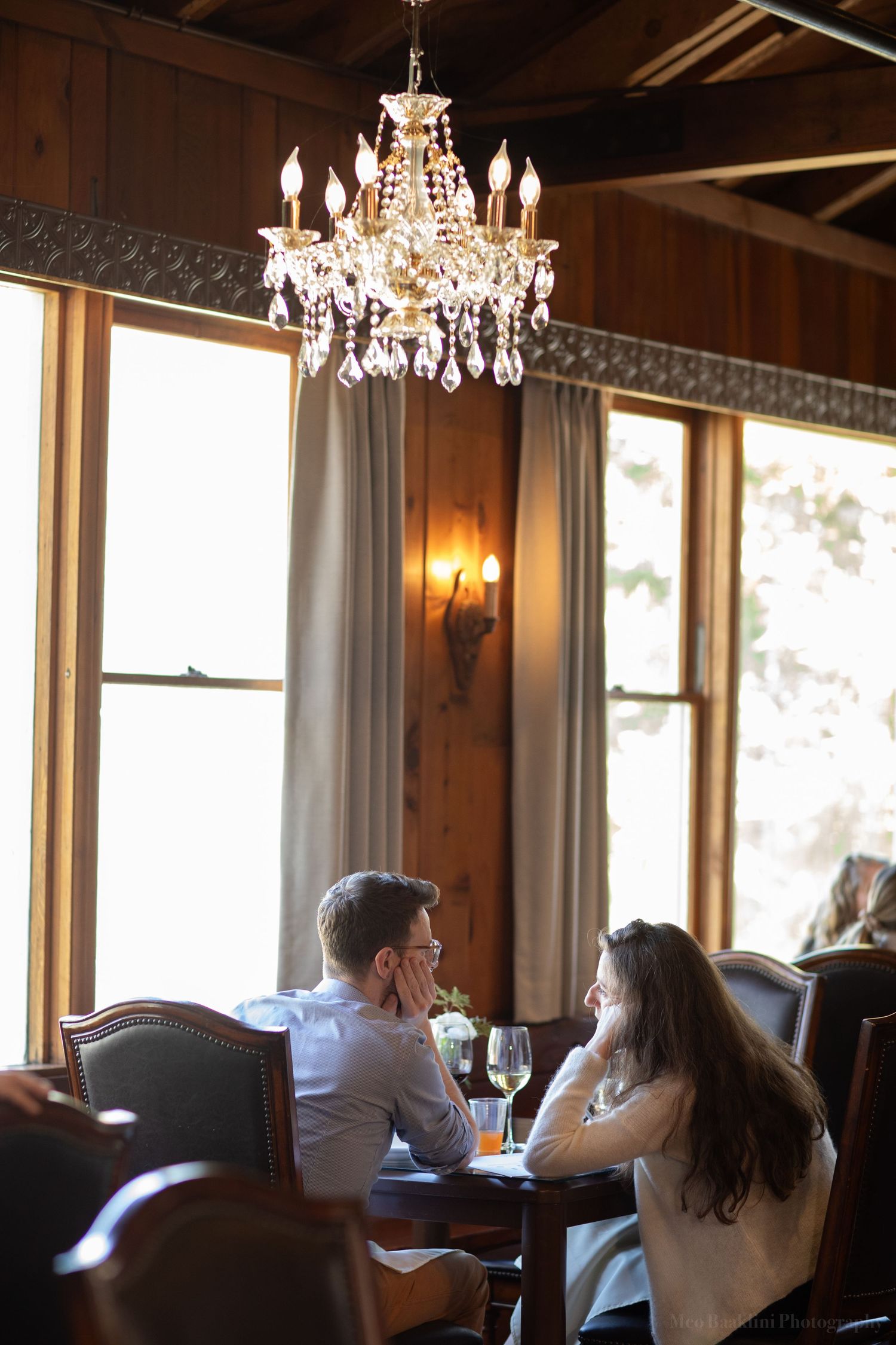 Romantic dining setting under crystal chandelier with natural light streaming through windows.