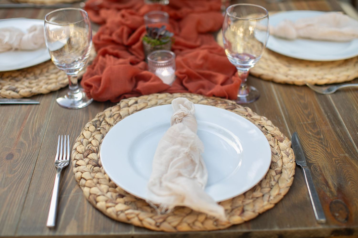 Place setting with woven charger plate, white napkin, and wine glass on wooden table.