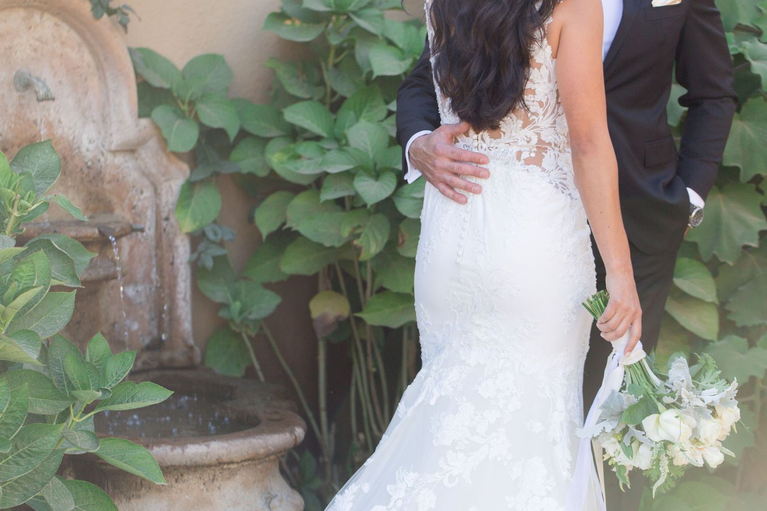 A close-up of a bride in a fitted lace gown holding a white bouquet.