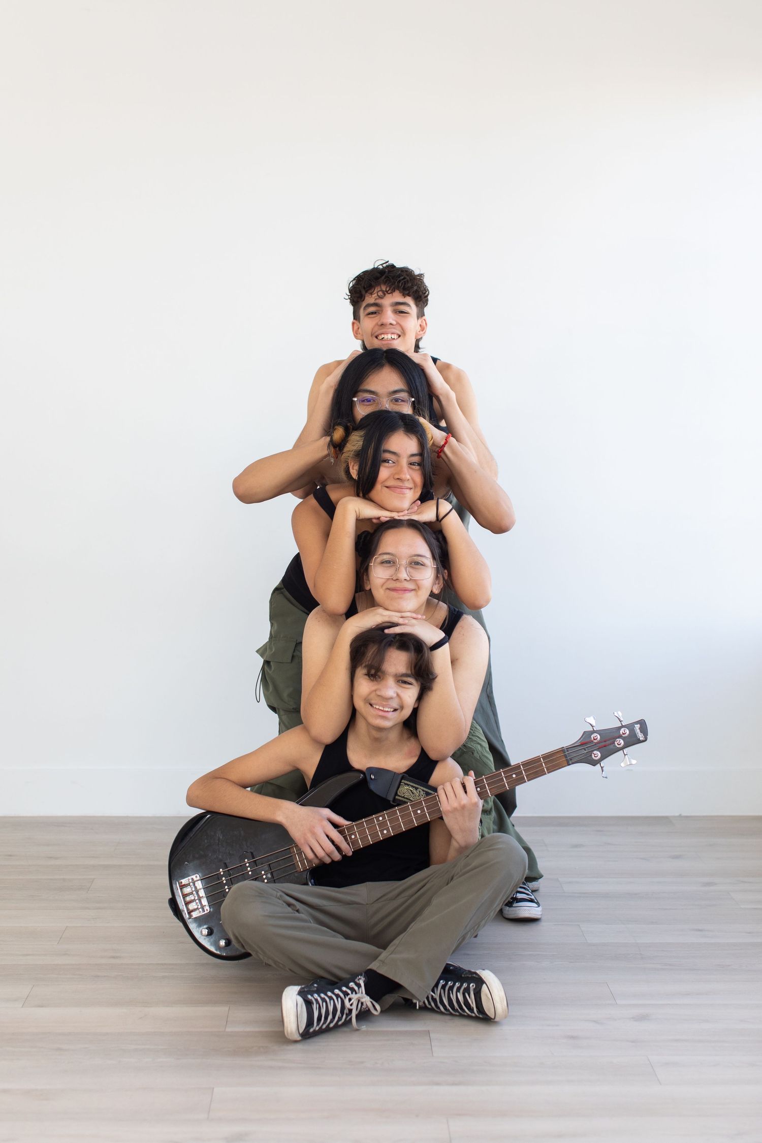 Musicians stack in a playful vertical pose while holding a bass guitar.