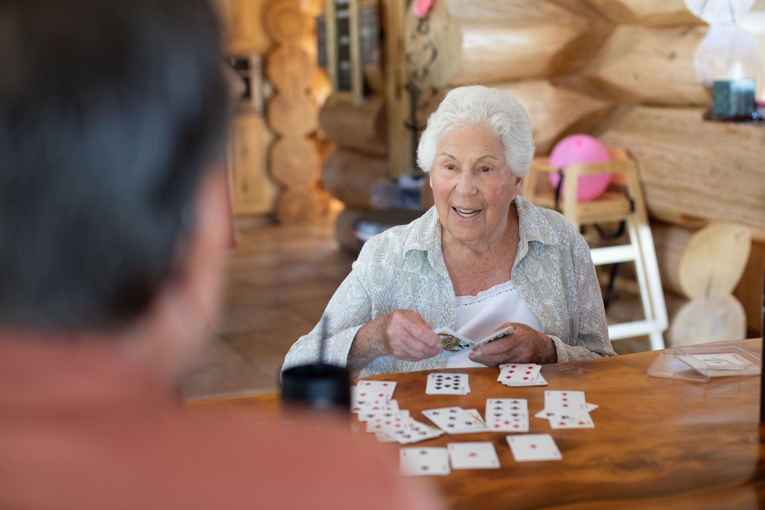 An elderly person playing cards in a cozy log cabin setting.
