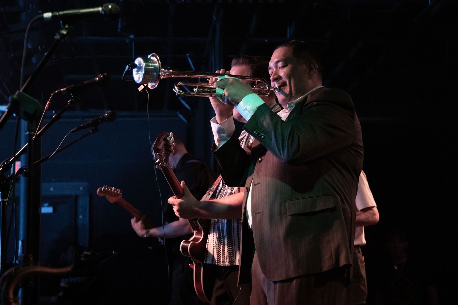 Jazz band performs with trumpet player in foreground under stage lights.
