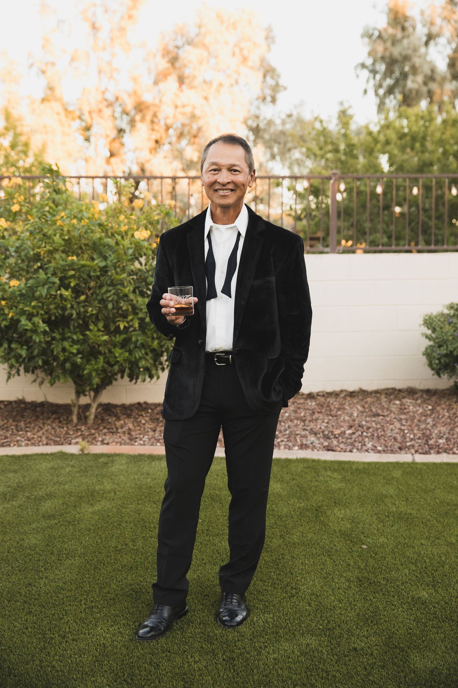 Figure in formal black suit standing on manicured lawn during golden hour.