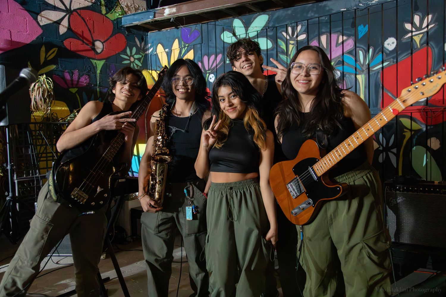 Band members pose with instruments against vibrant floral street art backdrop.