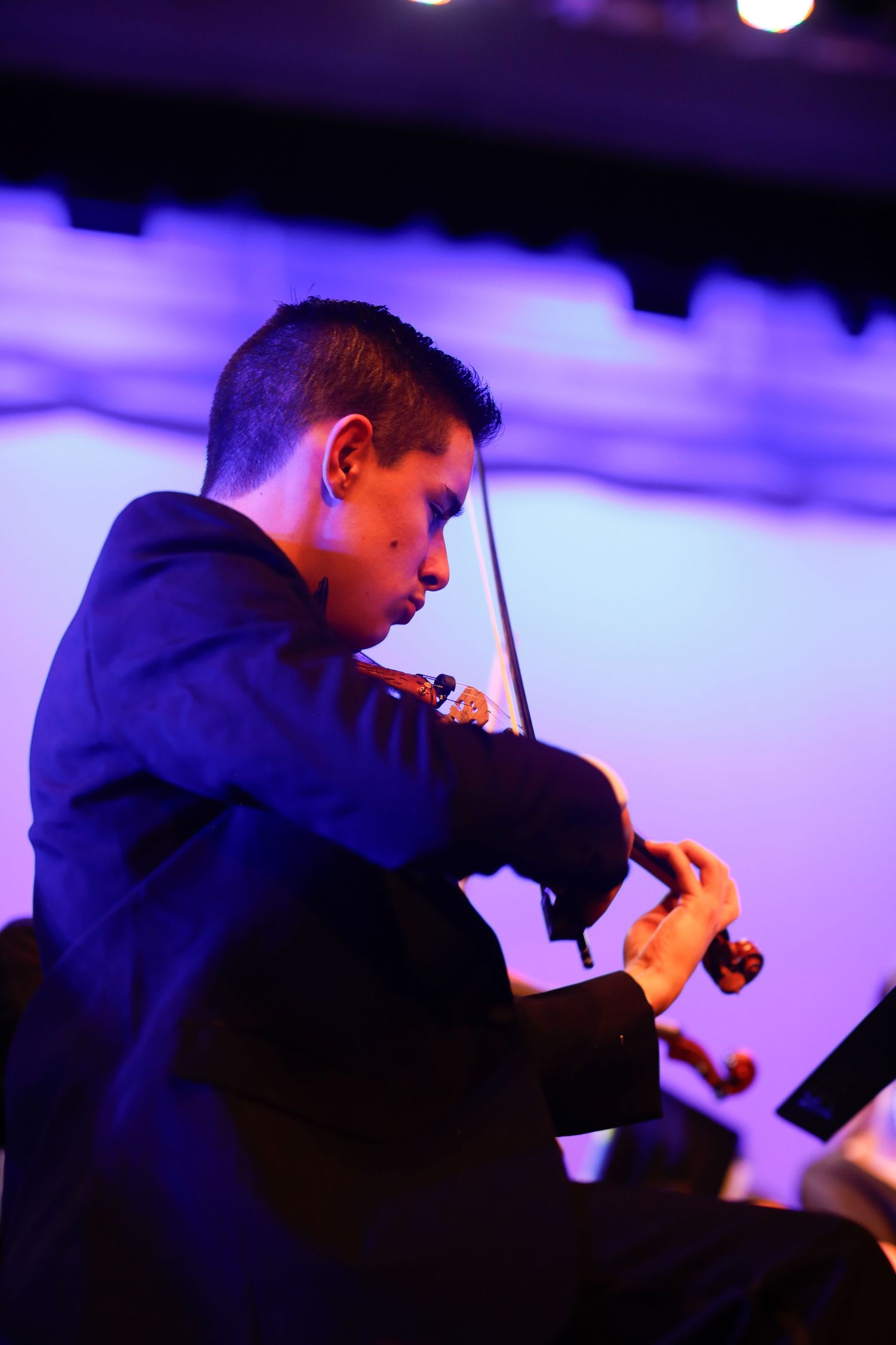 Violinist performing in dramatic blue stage lighting during concert.