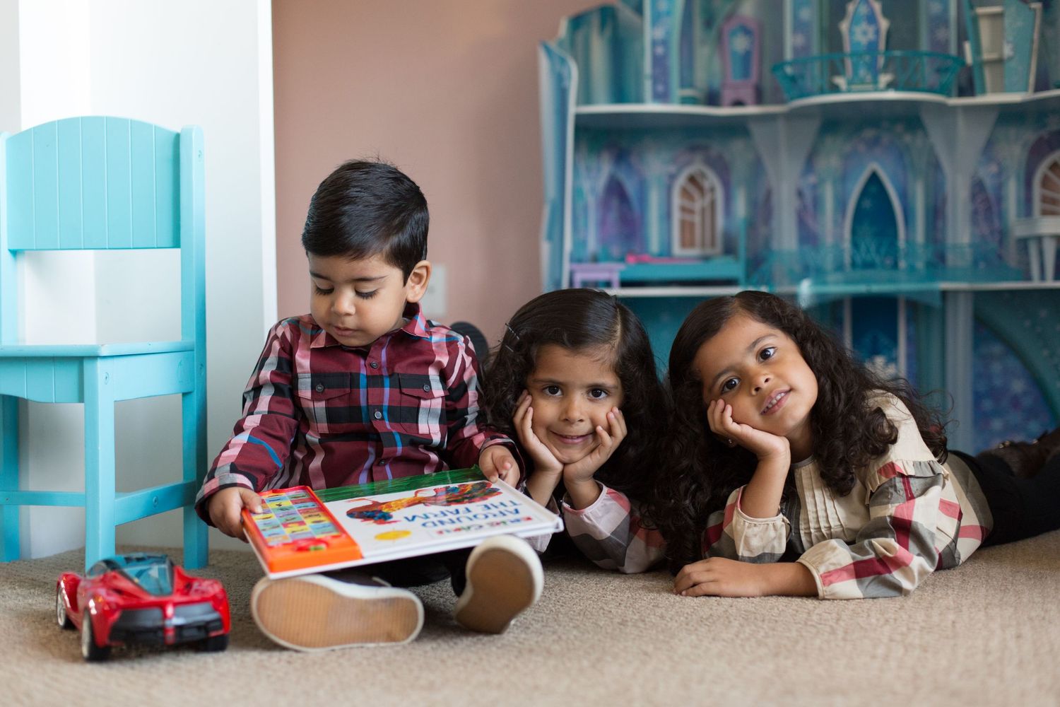 Children play with toys on carpet near blue chair and dollhouse.