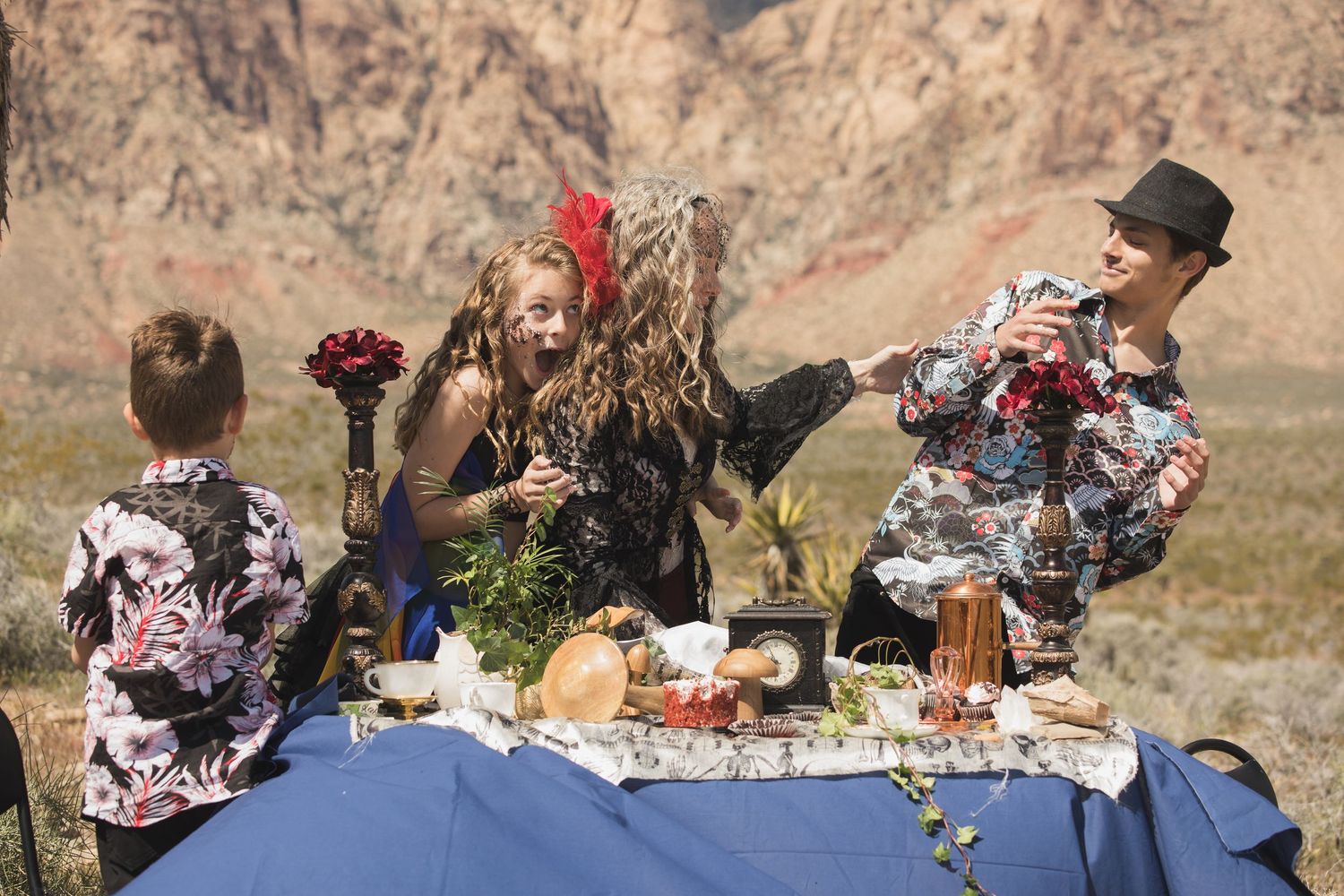 Tea party setup with food and drinks on blue tablecloth against dramatic desert canyon landscape.