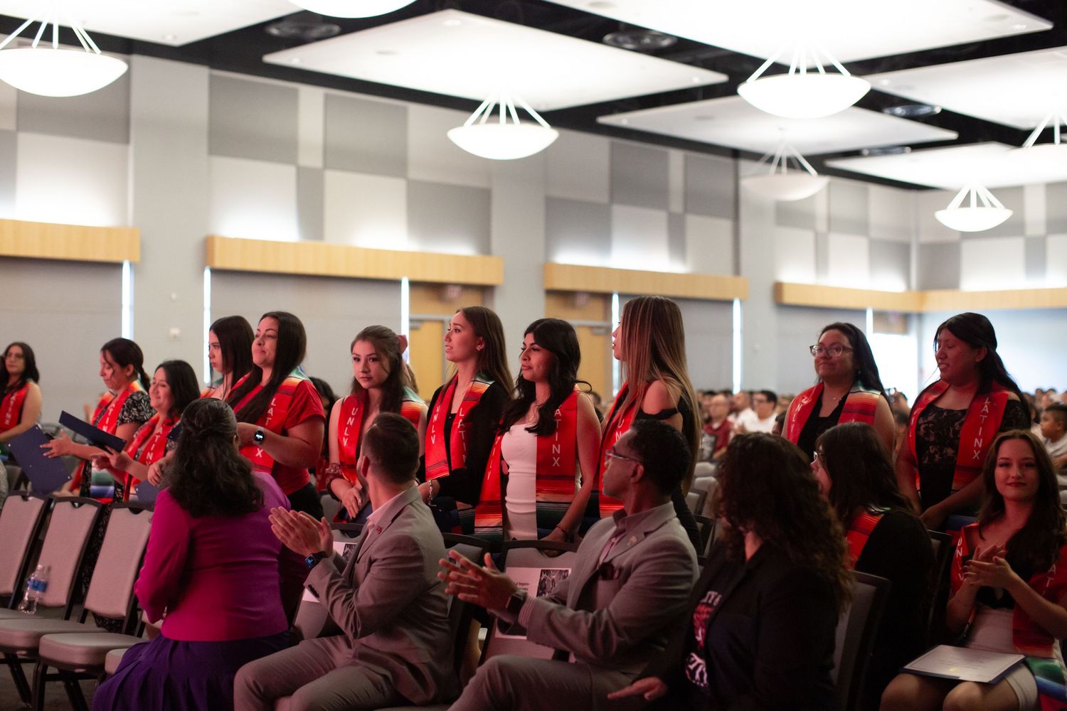 Audience members in red jackets seated in rows at an indoor event venue.