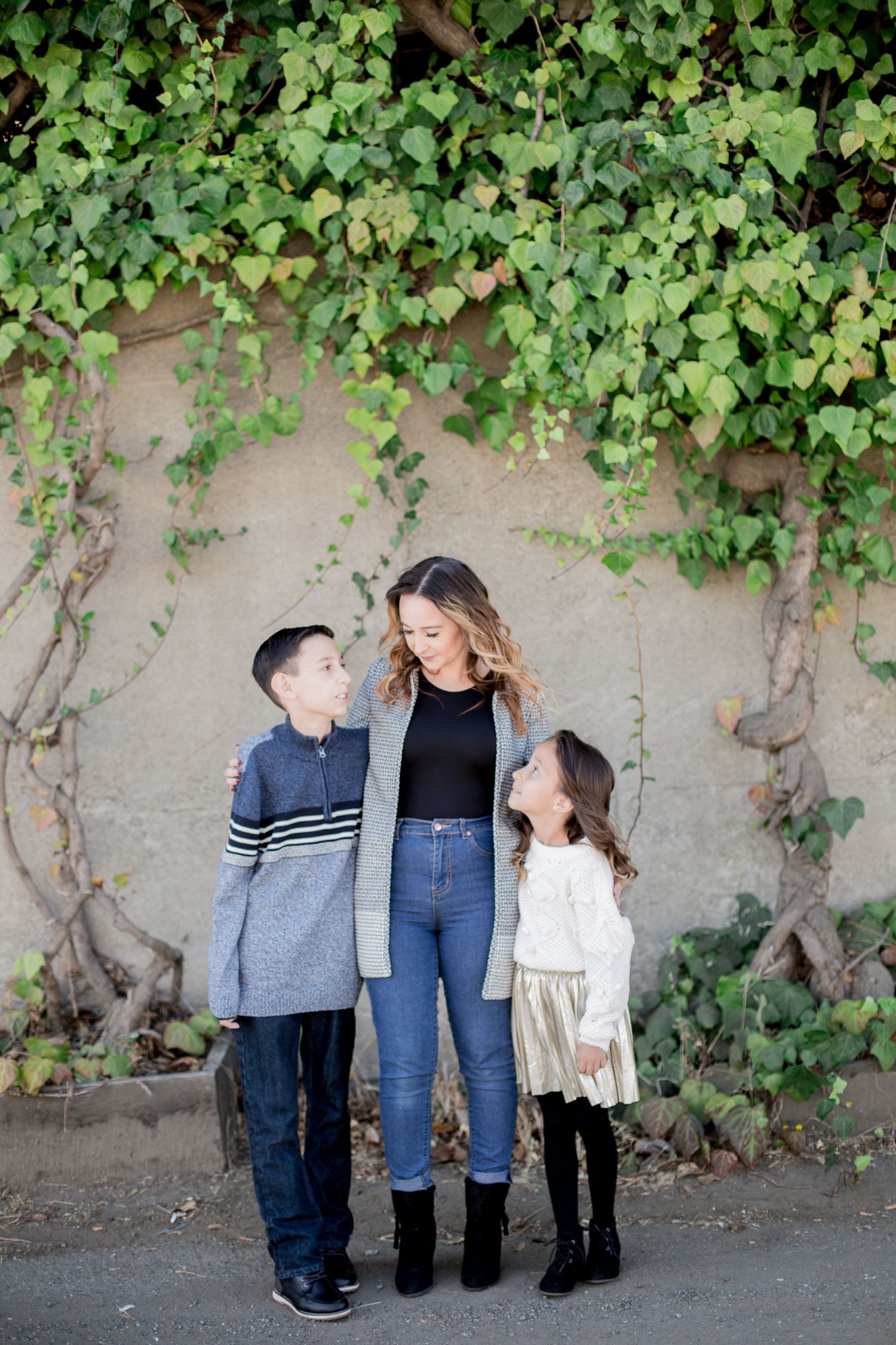 Family portraits against an ivy-covered wall in casual outfits.