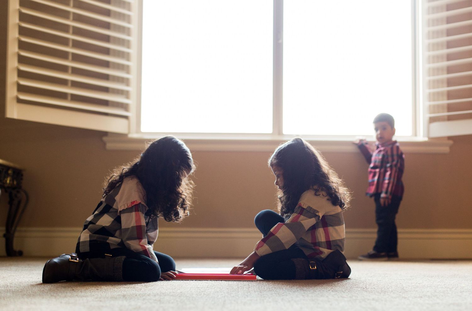 Three children play on carpet near window with sunlight streaming in.