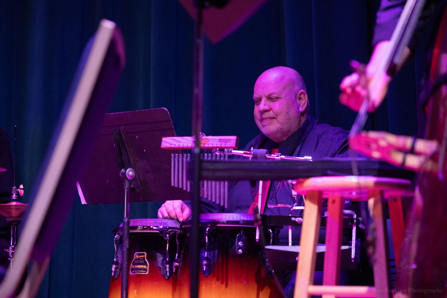 Drummer performing on stage with purple lighting and percussion setup.