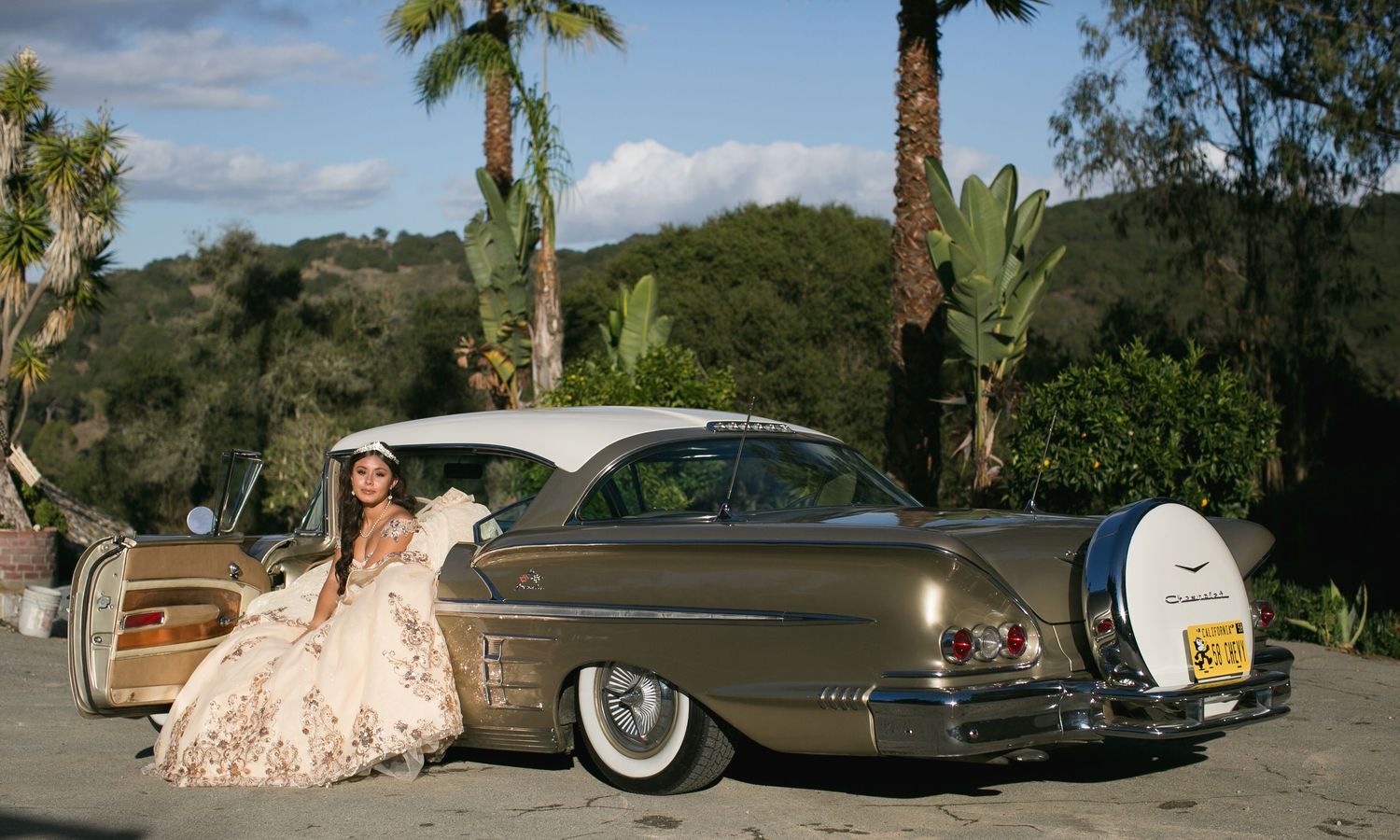 A classic bronze-colored vintage car parked with palm trees in the background.