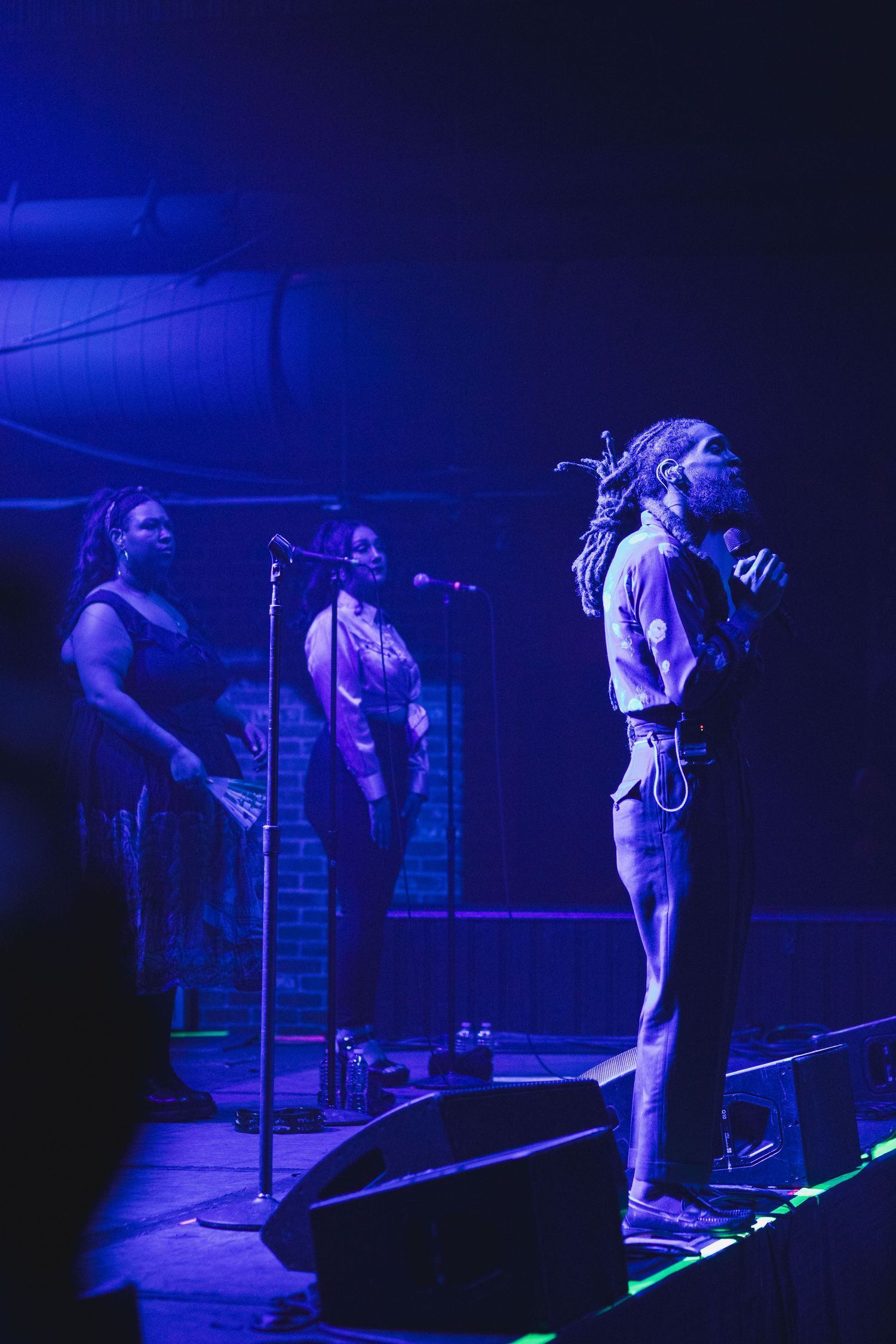 Musicians perform under blue stage lighting with microphones and dramatic backlighting effects.