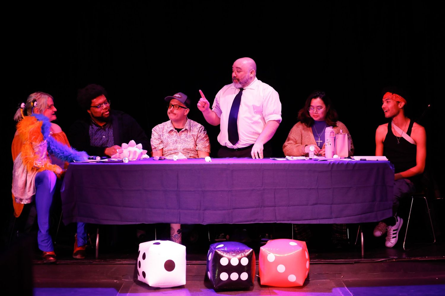 Stage performance featuring large dice props and performers under dramatic lighting.