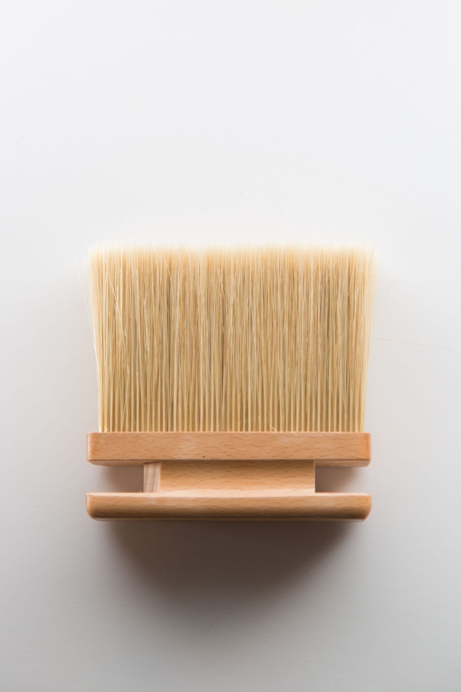 Close-up view of a clean wooden brush with light beige bristles against a white background.