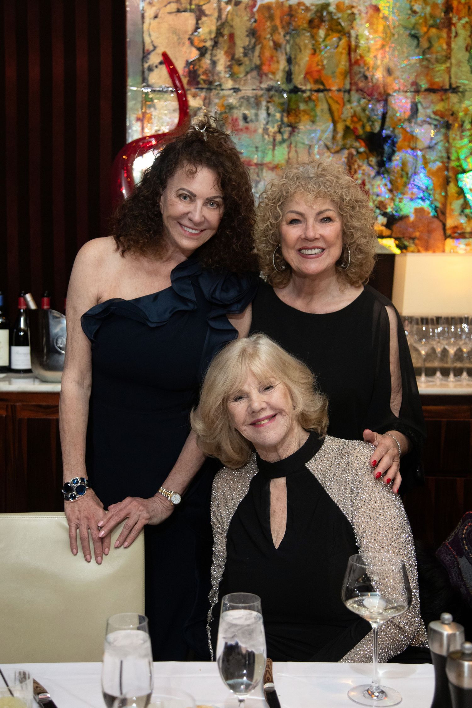 Friends pose together at an elegant dinner party with colorful abstract art in background.