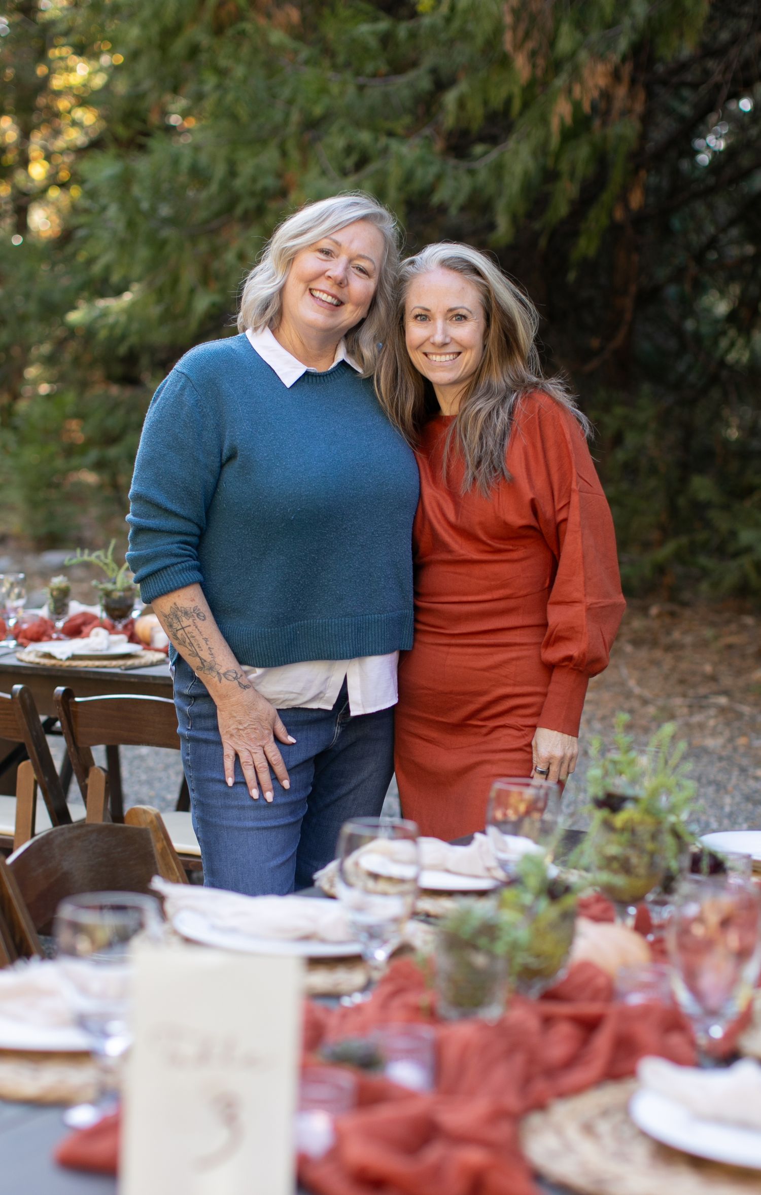 Outdoor dinner table setting in a forest with rustic decor and terracotta linens.