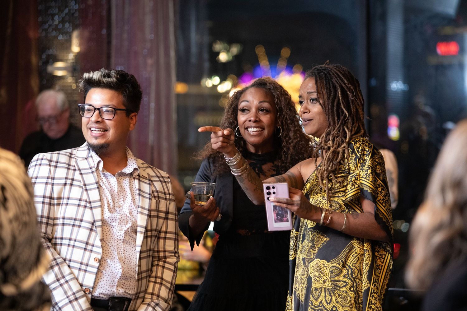 Three guests share laughs and drinks during a lively evening celebration.