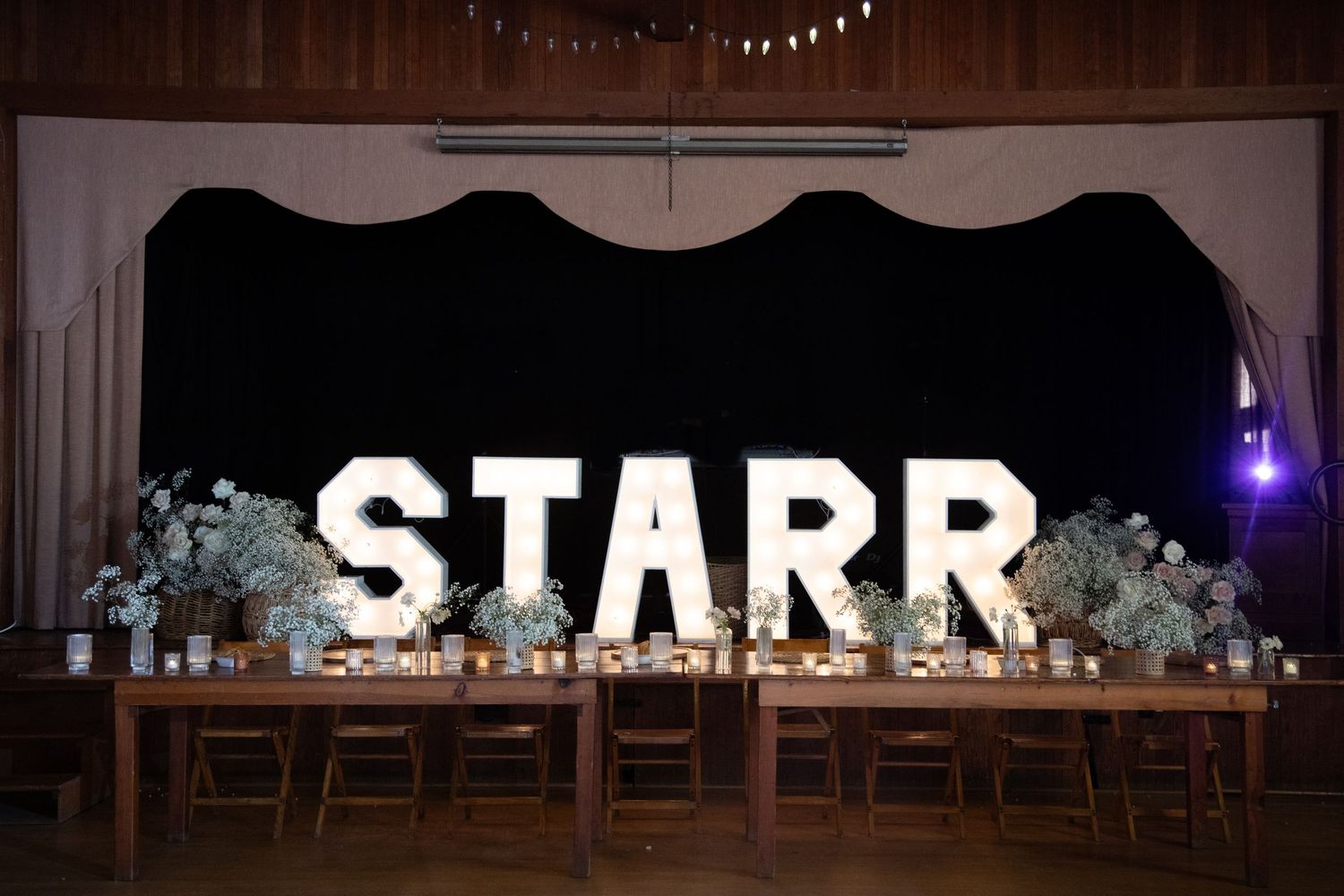 Illuminated STARR marquee letters with floral arrangements on a dark backdrop at an event.