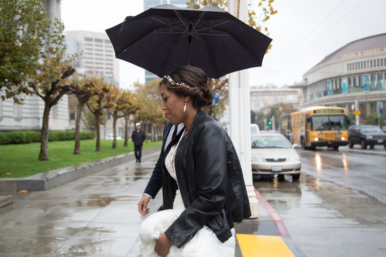 People walking under umbrellas on a rainy city street with buses and cars visible in the background.