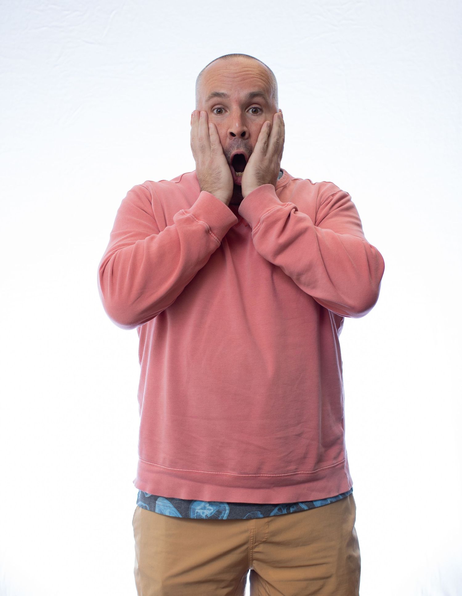 Person in salmon-colored sweater covering face with hands in shocked expression.