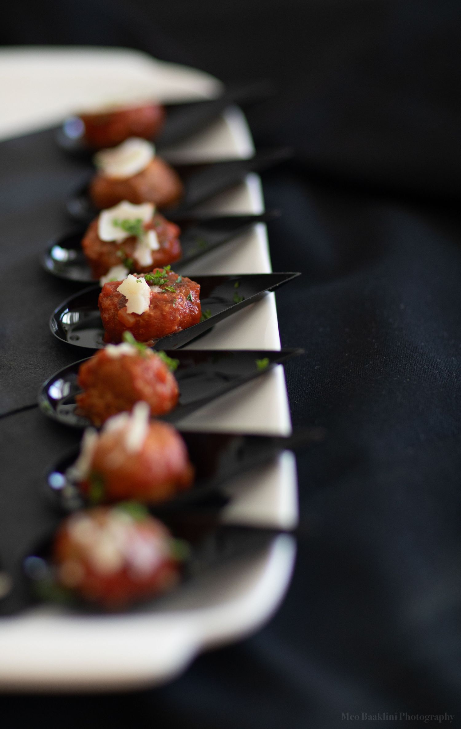 Row of elegantly plated appetizers on black spoons with garnish.