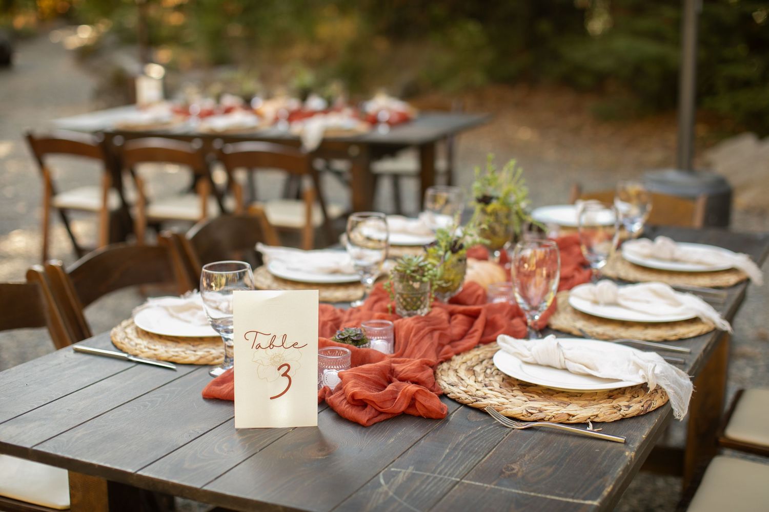 Rustic outdoor wedding table setup with terracotta accents and table numbers.