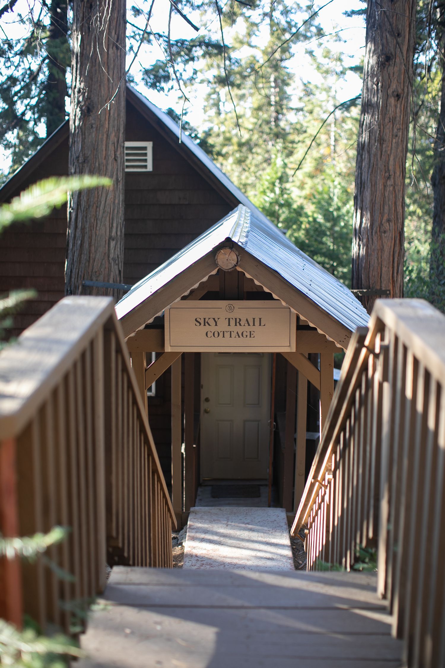 Wooden walkway leading to Sky Trail cottage buildings in a forest setting.