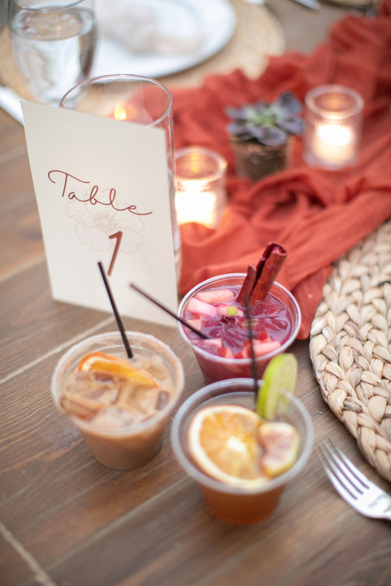 Table settings with colorful cocktails and table number cards at an outdoor event.