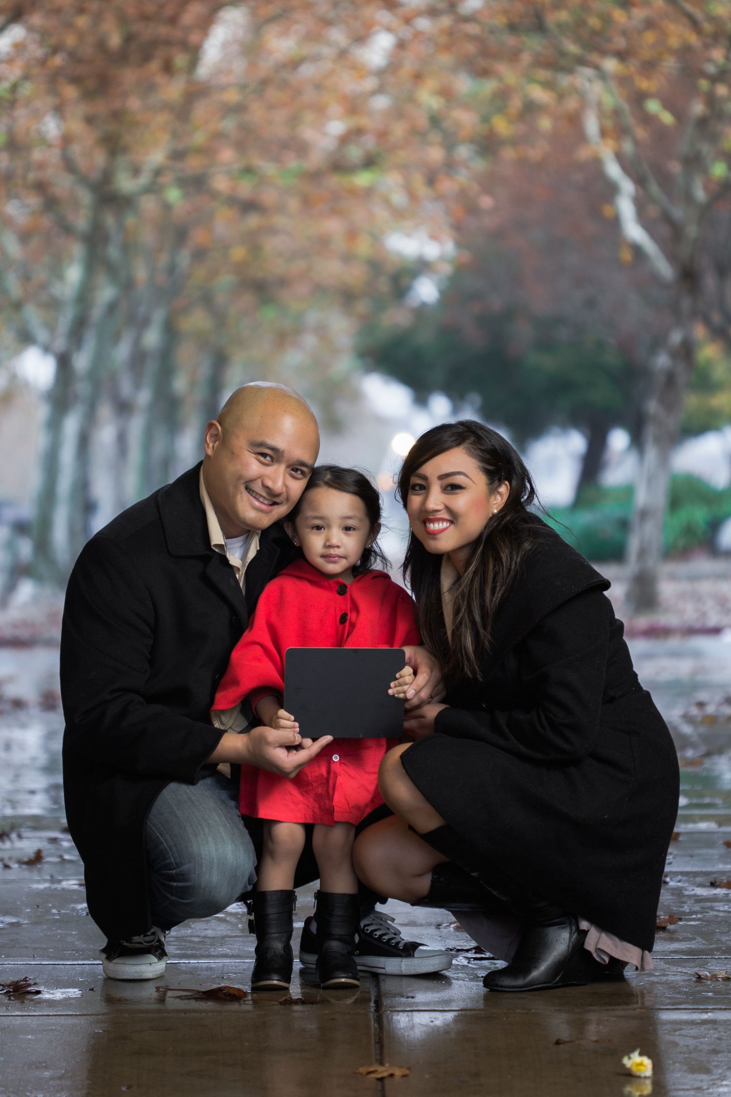 Family autumn portrait with child in red coat holding tablet device.