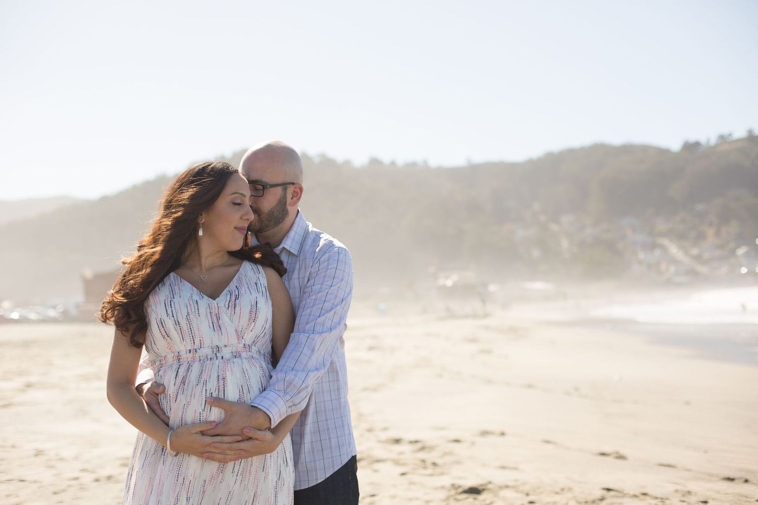 Romantic maternity photoshoot on sandy beach during golden hour.
