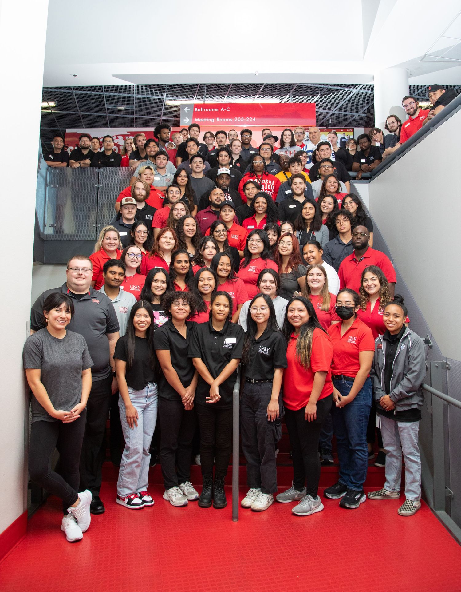 A large group photo of staff and students wearing red and black uniforms on stairs.